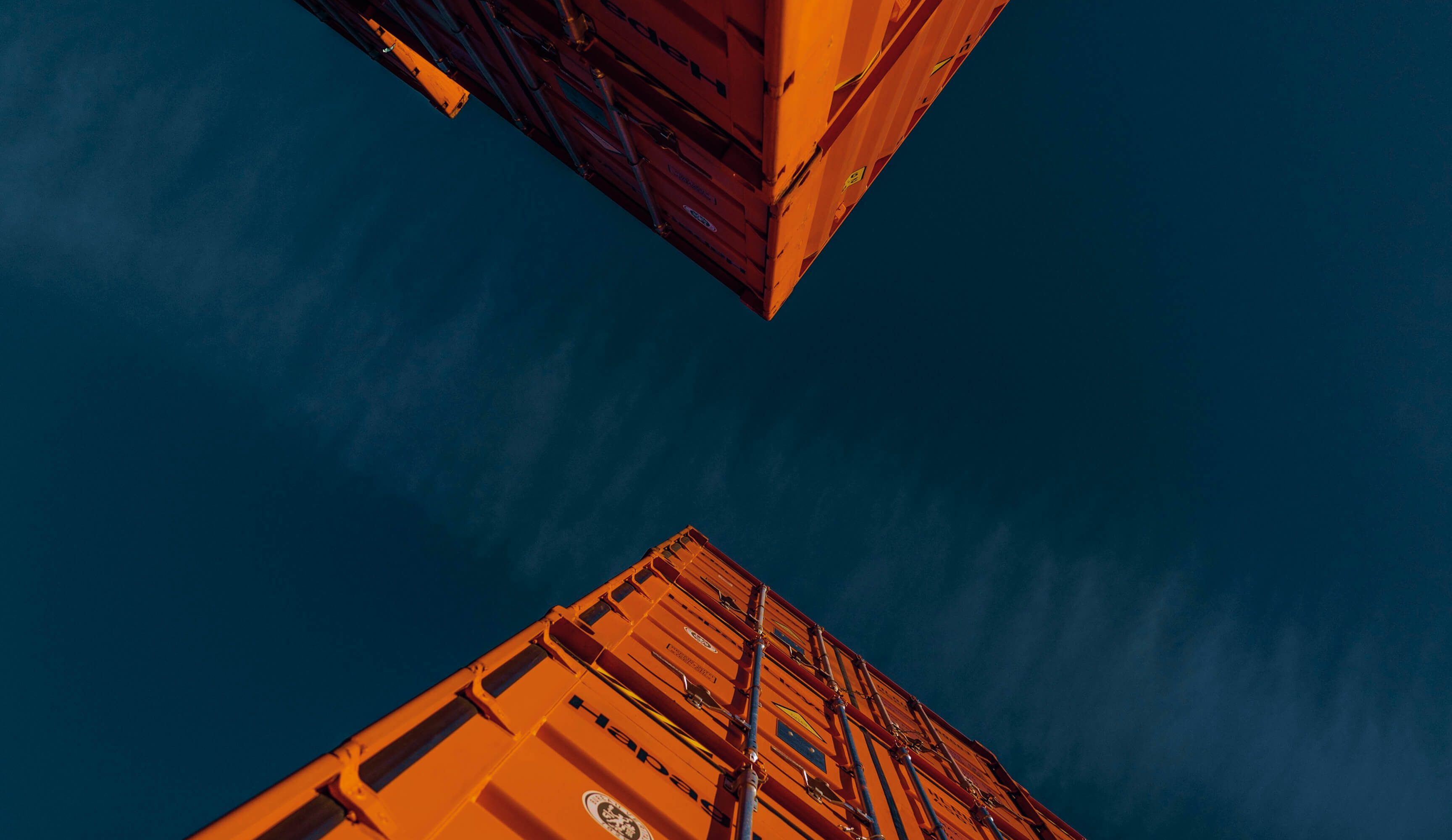 View looking up at two orange shipping containers against a deep blue sky.